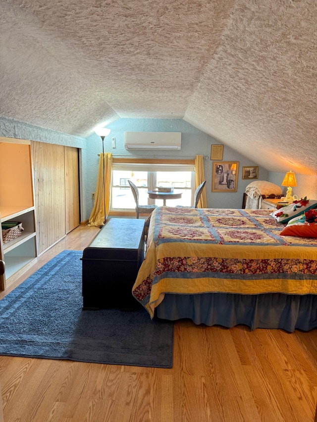 bedroom with lofted ceiling, wood finished floors, a wall mounted air conditioner, and a textured ceiling