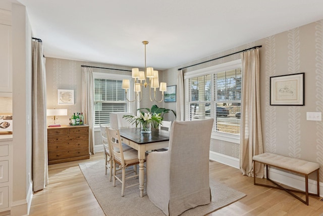 dining room with light wood finished floors, a chandelier, wallpapered walls, and baseboards