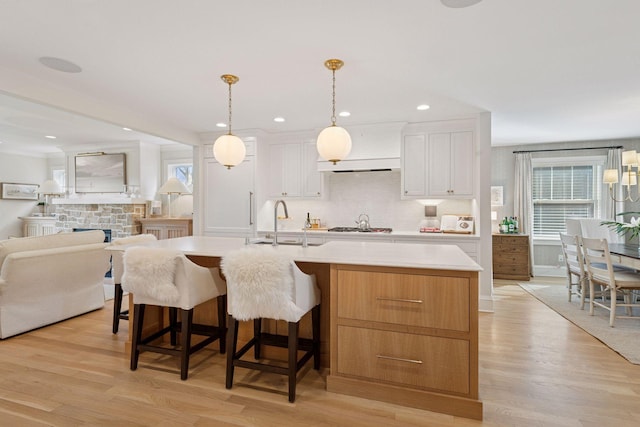 kitchen with backsplash, light countertops, light wood-type flooring, white cabinetry, and a sink