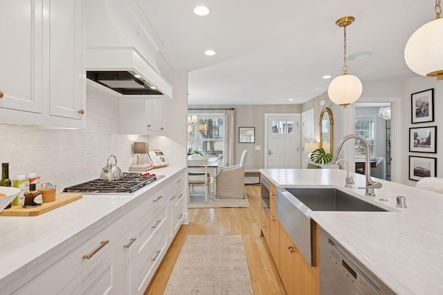 kitchen with light wood-style flooring, a sink, hanging light fixtures, light countertops, and stainless steel appliances