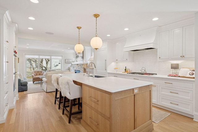 kitchen featuring stainless steel gas cooktop, light wood-style flooring, a sink, custom range hood, and open floor plan