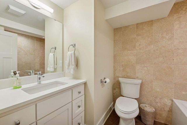 bathroom with visible vents, a washtub, toilet, vanity, and tile walls