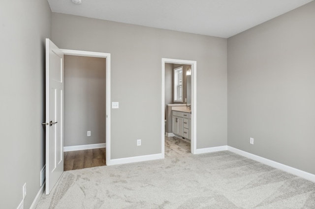 unfurnished bedroom with light colored carpet, connected bathroom, and baseboards