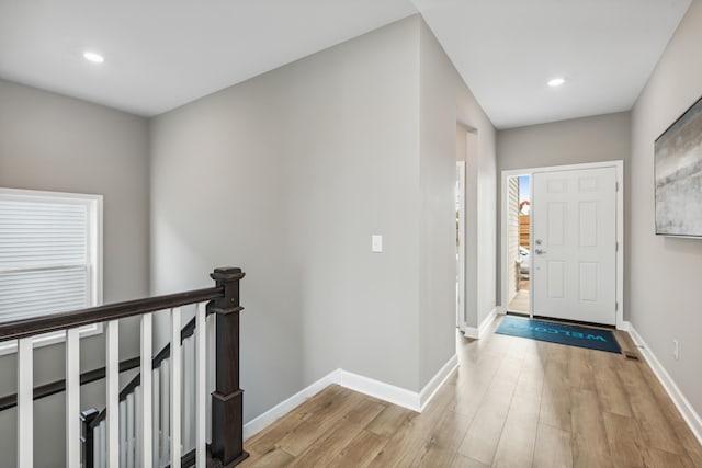 hall with an upstairs landing, recessed lighting, light wood-type flooring, and baseboards