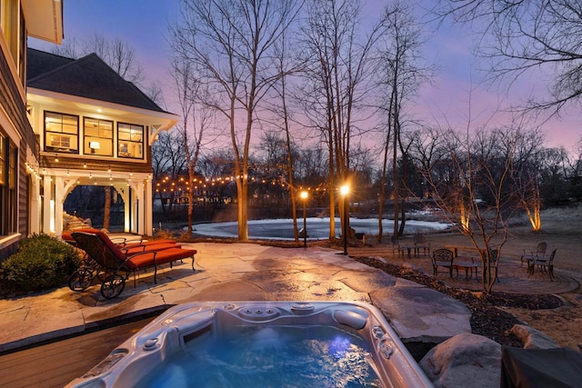 pool at dusk featuring a patio and an outdoor hot tub