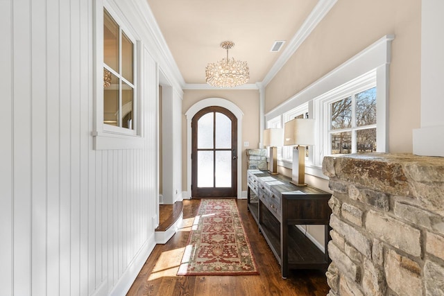 foyer with visible vents, a notable chandelier, wood finished floors, arched walkways, and crown molding