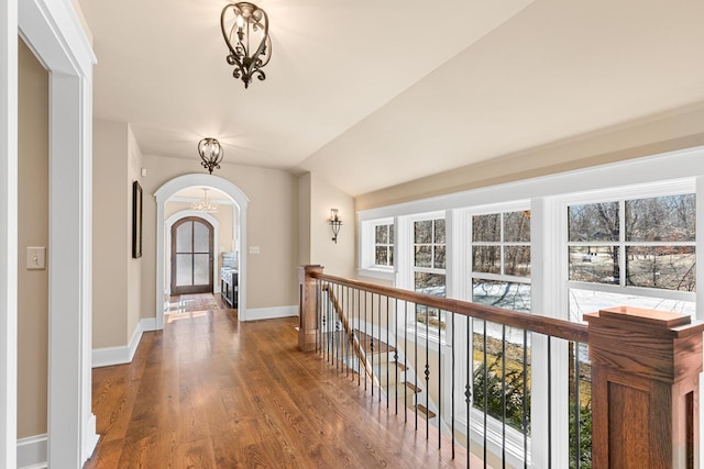 corridor featuring baseboards, vaulted ceiling, wood finished floors, arched walkways, and a notable chandelier