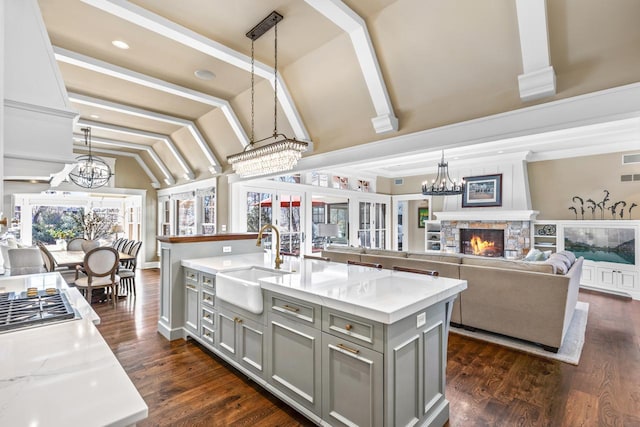 kitchen with a sink, vaulted ceiling, gray cabinets, an inviting chandelier, and a kitchen island with sink