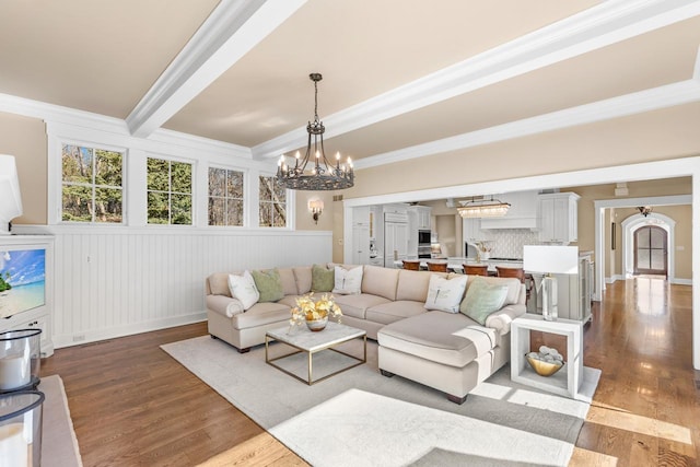 living area with beamed ceiling, a notable chandelier, wood finished floors, and crown molding