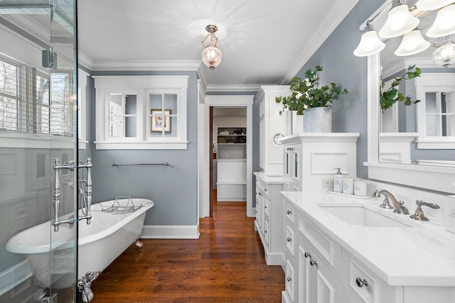 bathroom with ornamental molding, an inviting chandelier, wood finished floors, a soaking tub, and vanity