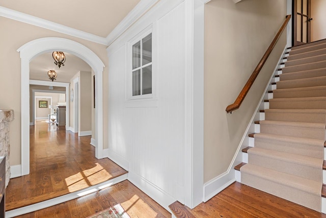 corridor featuring wood finished floors, baseboards, arched walkways, ornamental molding, and stairs