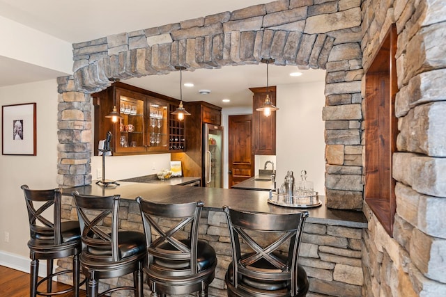 bar featuring dark wood-type flooring, indoor wet bar, hanging light fixtures, stainless steel fridge, and a sink