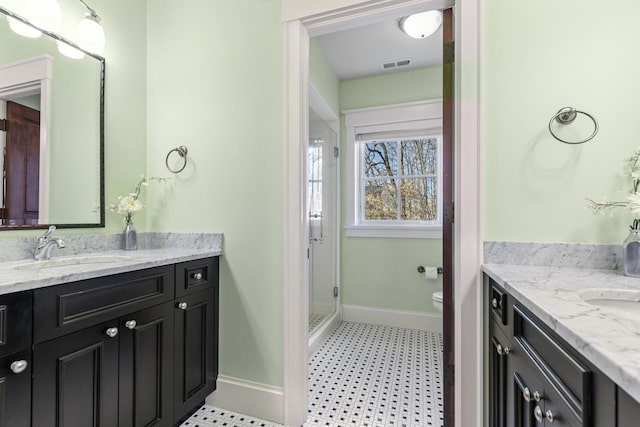 full bath featuring visible vents, two vanities, a stall shower, a sink, and baseboards