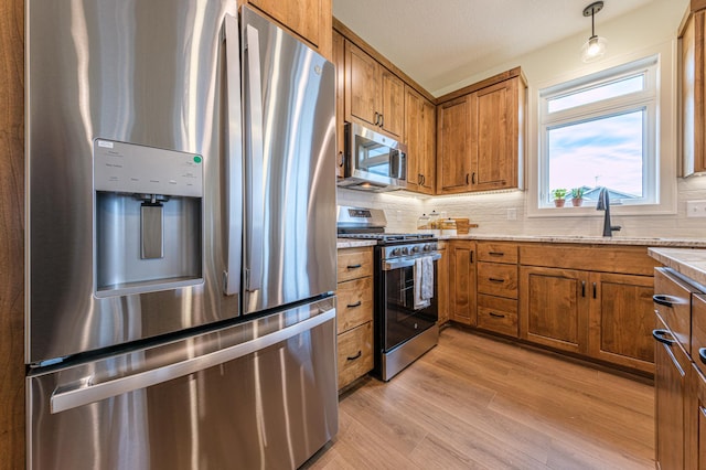 kitchen with light wood finished floors, decorative backsplash, brown cabinetry, stainless steel appliances, and a sink