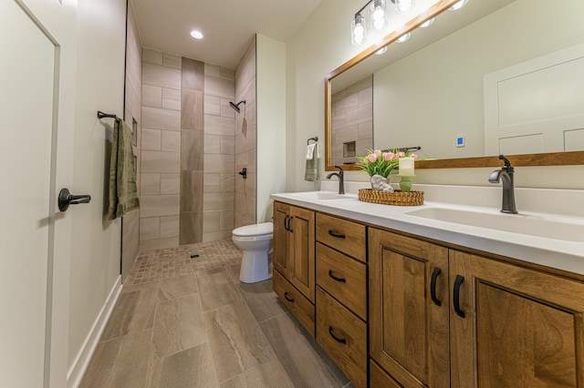 full bathroom featuring double vanity, tiled shower, toilet, and a sink
