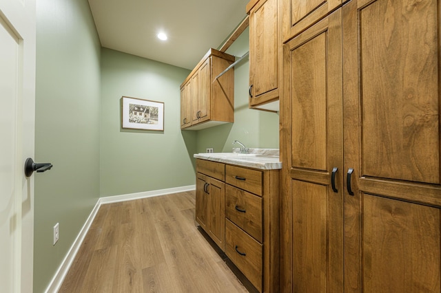 laundry area featuring a sink, baseboards, and light wood-style flooring