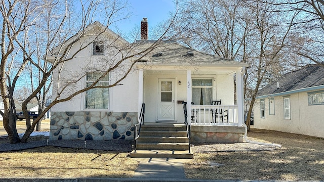 view of front of house featuring a shingled roof, a porch, stucco siding, a chimney, and stone siding