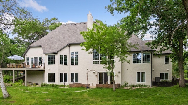 back of house with a lawn, a chimney, roof with shingles, and stucco siding