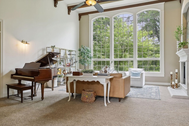 sitting room with a ceiling fan, baseboards, carpet floors, a fireplace with raised hearth, and beamed ceiling