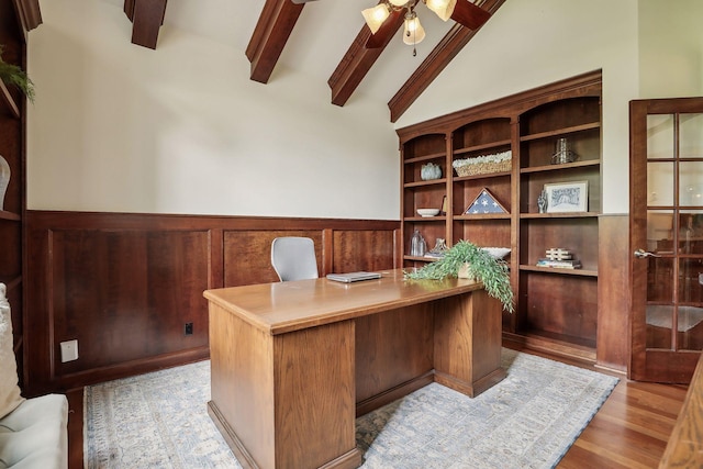 office with light wood-type flooring, a wainscoted wall, a ceiling fan, and vaulted ceiling with beams