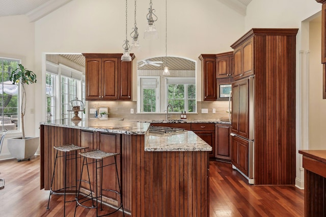 kitchen featuring light stone counters, dark wood finished floors, paneled built in fridge, decorative backsplash, and a kitchen breakfast bar