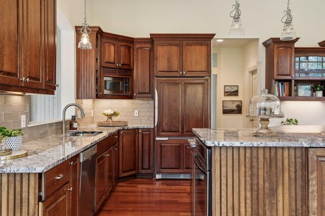 kitchen featuring tasteful backsplash, a sink, light stone countertops, built in appliances, and dark wood-style flooring