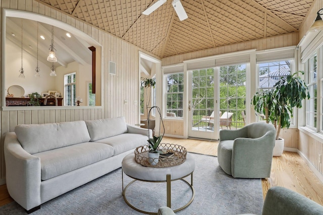 living room with high vaulted ceiling, wood finished floors, a ceiling fan, and wood walls