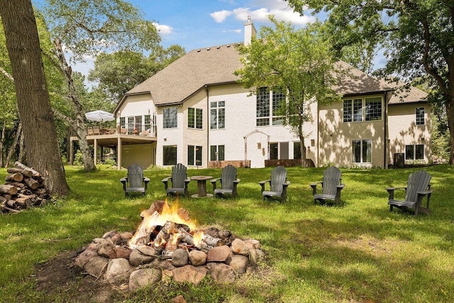 rear view of property featuring a chimney, a lawn, and an outdoor fire pit