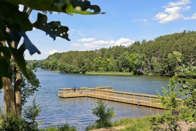 view of dock with a wooded view and a water view