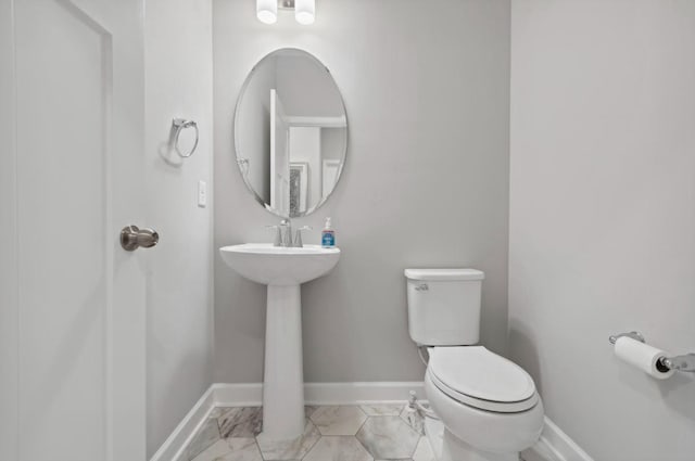 half bathroom with marble finish floor, toilet, and baseboards