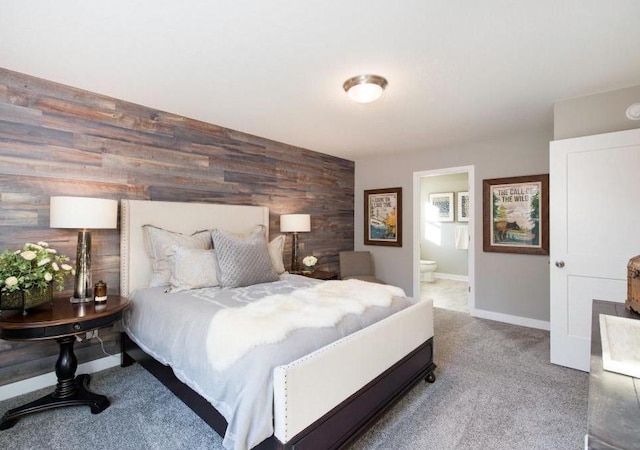 bedroom featuring connected bathroom, carpet, wood walls, baseboards, and an accent wall