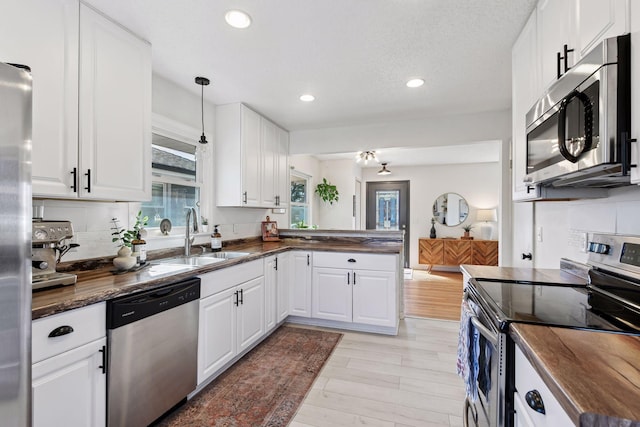 kitchen with a peninsula, a sink, white cabinets, appliances with stainless steel finishes, and tasteful backsplash