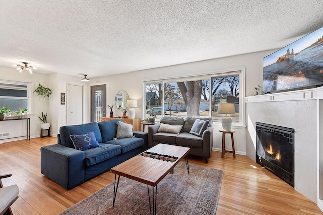 living area featuring a glass covered fireplace, a textured ceiling, and light wood-type flooring