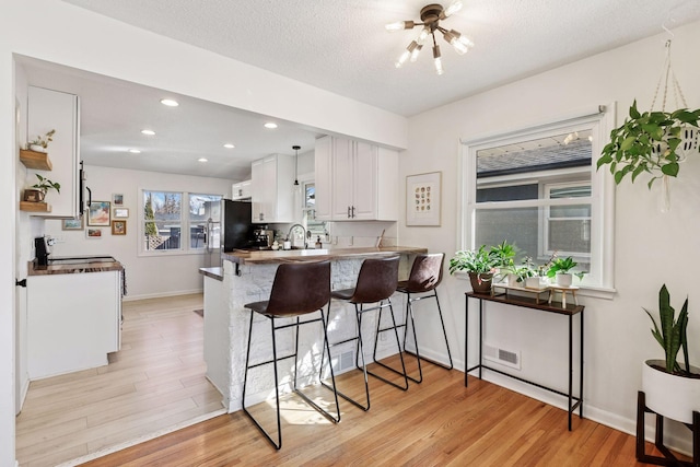 kitchen featuring visible vents, a kitchen bar, white cabinetry, light wood-style floors, and a peninsula