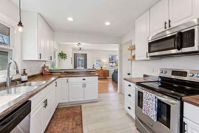 kitchen featuring a peninsula, a sink, stainless steel appliances, wood counters, and white cabinetry