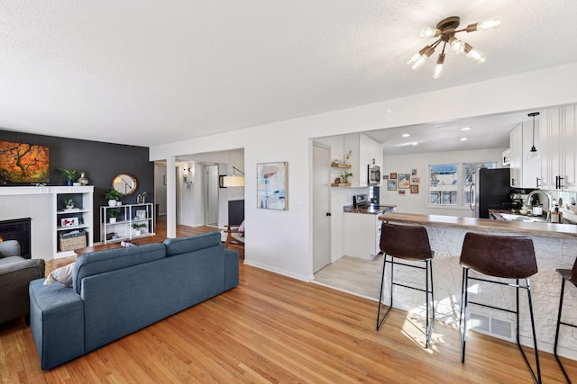 living room featuring a tiled fireplace, recessed lighting, light wood-style floors, and a textured ceiling