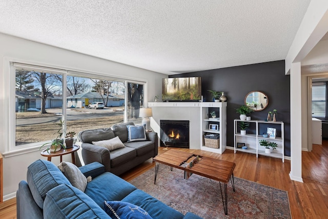 living room with a tile fireplace, a textured ceiling, and wood finished floors