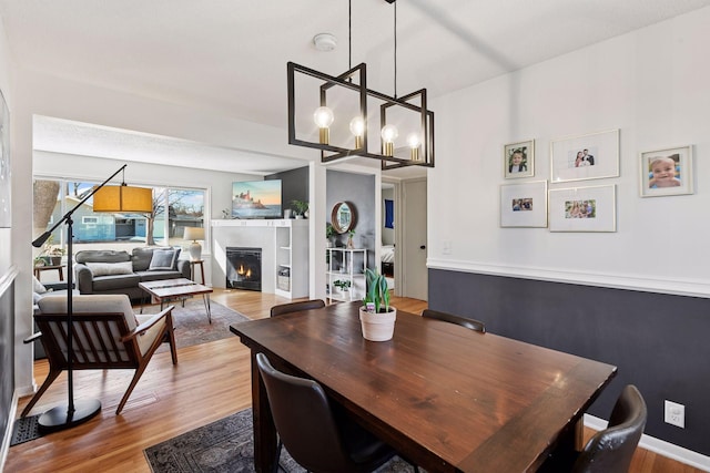 dining area featuring a chandelier, a warm lit fireplace, and wood finished floors