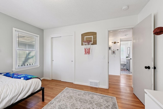 bedroom featuring visible vents, baseboards, light wood-type flooring, a closet, and a textured ceiling