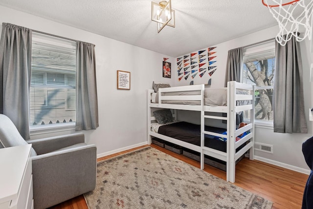 bedroom featuring visible vents, baseboards, a textured ceiling, and wood finished floors