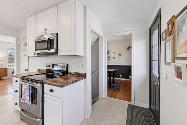 kitchen with light wood-style flooring, stainless steel appliances, baseboards, white cabinets, and lofted ceiling