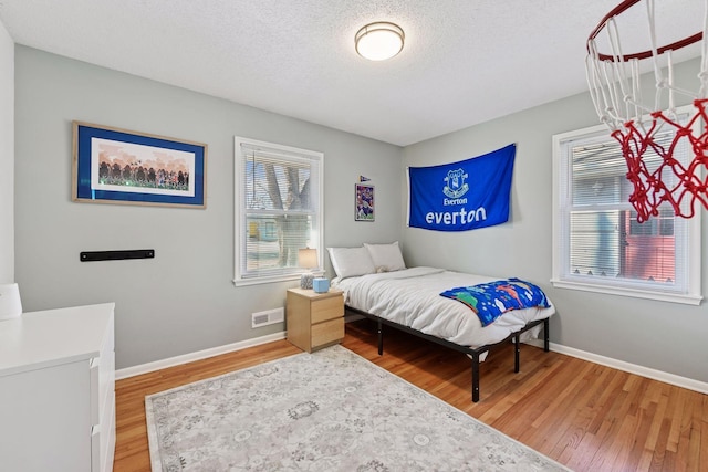 bedroom with visible vents, a textured ceiling, light wood-type flooring, and baseboards