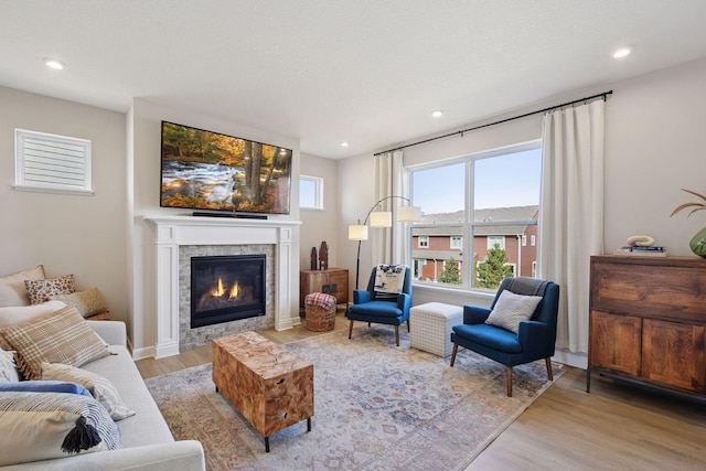 living area featuring a glass covered fireplace, recessed lighting, light wood-type flooring, and baseboards