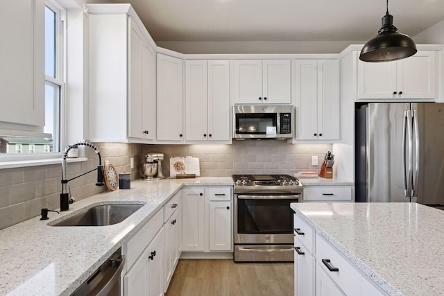 kitchen featuring light wood-style flooring, a sink, backsplash, appliances with stainless steel finishes, and white cabinets