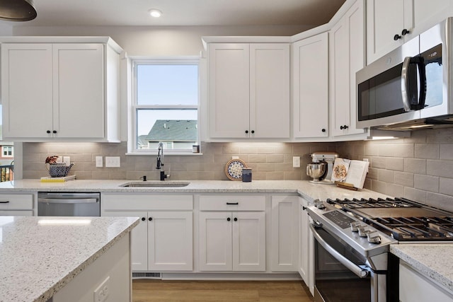 kitchen featuring visible vents, light stone counters, stainless steel appliances, white cabinetry, and a sink