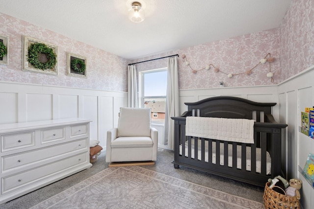 bedroom with a wainscoted wall, a crib, wallpapered walls, and carpet floors