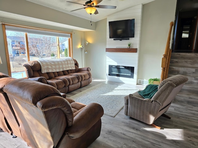 living area with wood finished floors, visible vents, lofted ceiling, ceiling fan, and a large fireplace