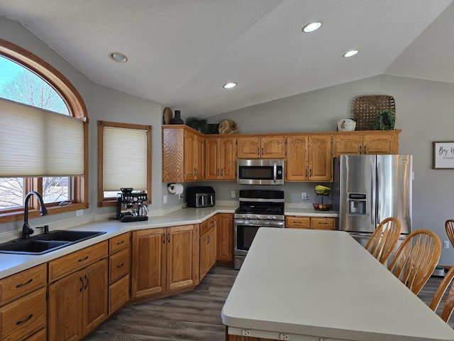 kitchen with a sink, a kitchen island, stainless steel appliances, light countertops, and vaulted ceiling