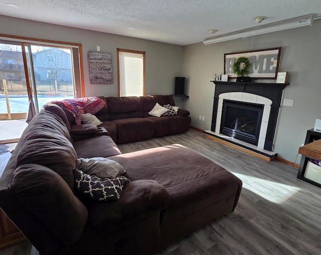 living area with baseboards, a textured ceiling, wood finished floors, and a tile fireplace