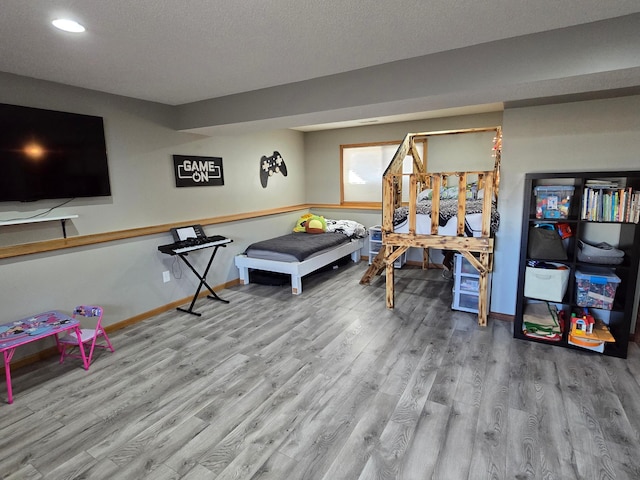 game room featuring a textured ceiling, baseboards, and wood finished floors